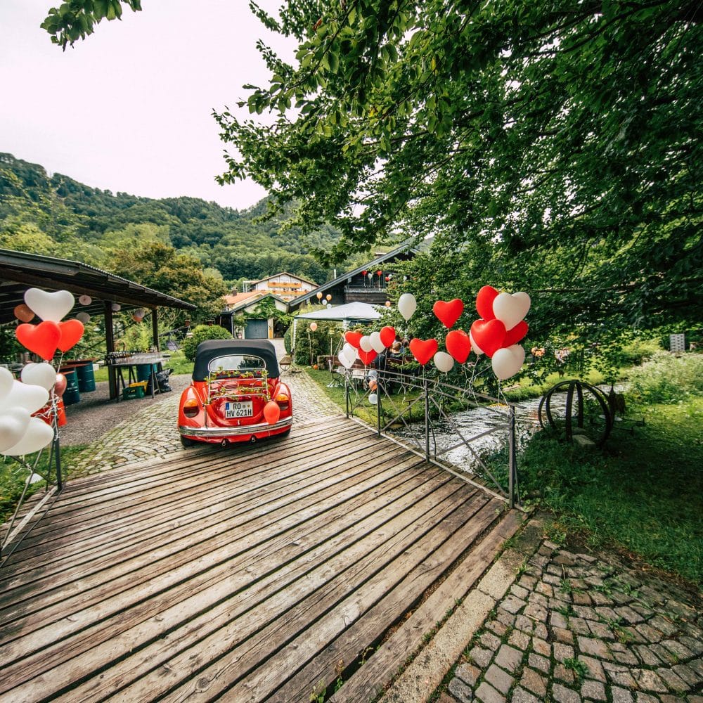 Ein roter VW Käfer als Hochzeitswagen fährt über eine Brücke, Herzluftballons, Hochzeit, Event Fotografie, WINGMEN Media